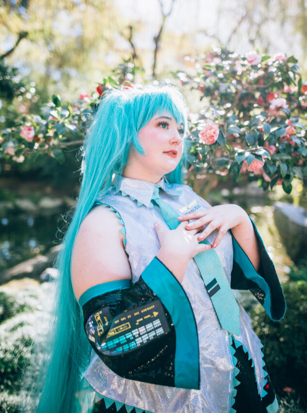 Hatsune Miku Cosplayer in front of greenery and camelias, looking wistfully to the right